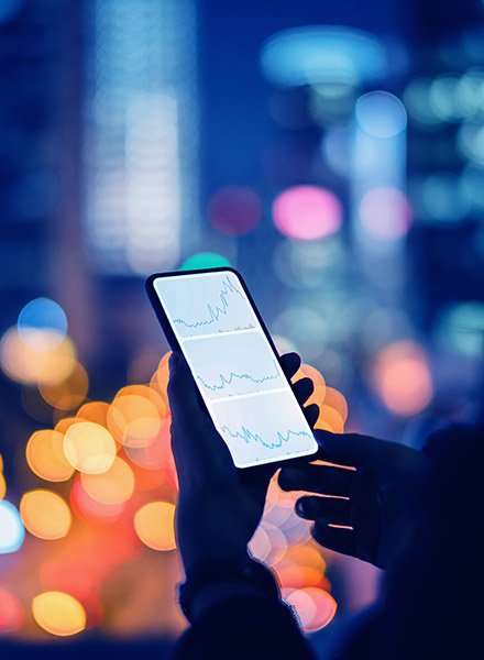 A person is looking at their phone viewing the stock market with a city skyline behind them.