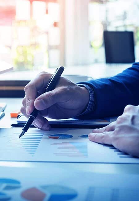 A person is using a fountain pen to mark up a color print out of pie charts and bar graphs.
