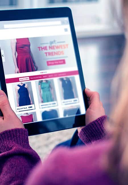 A woman is golding a tablet going clothing shopping.